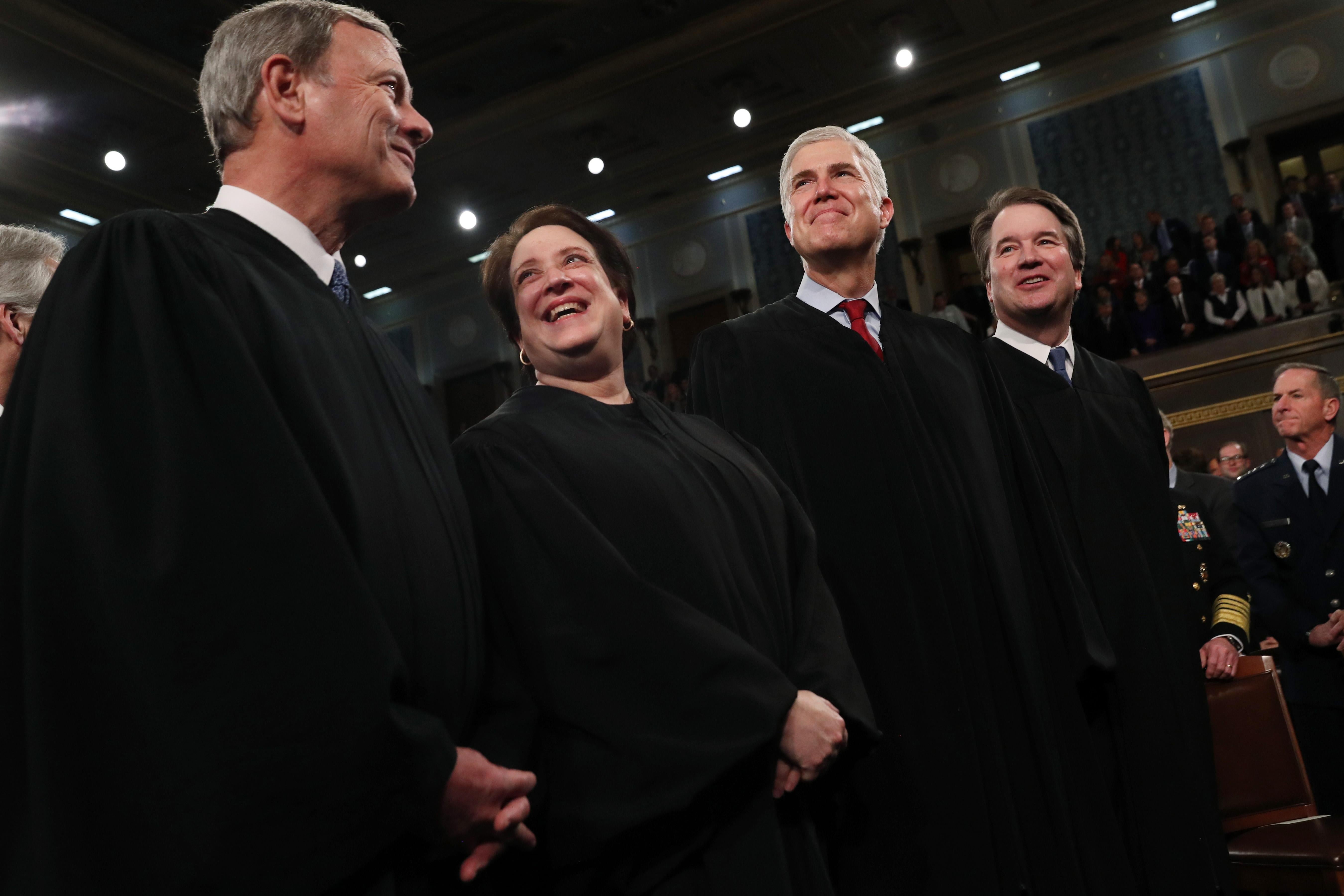 Supreme Court justices John Roberts, Elena Kagan, Neil Gorsuch and Brett Kavanaugh smile at each other while standing.