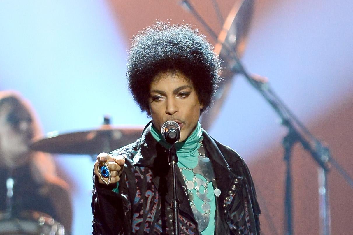 Prince stands in front of a microphone, points toward the camera.