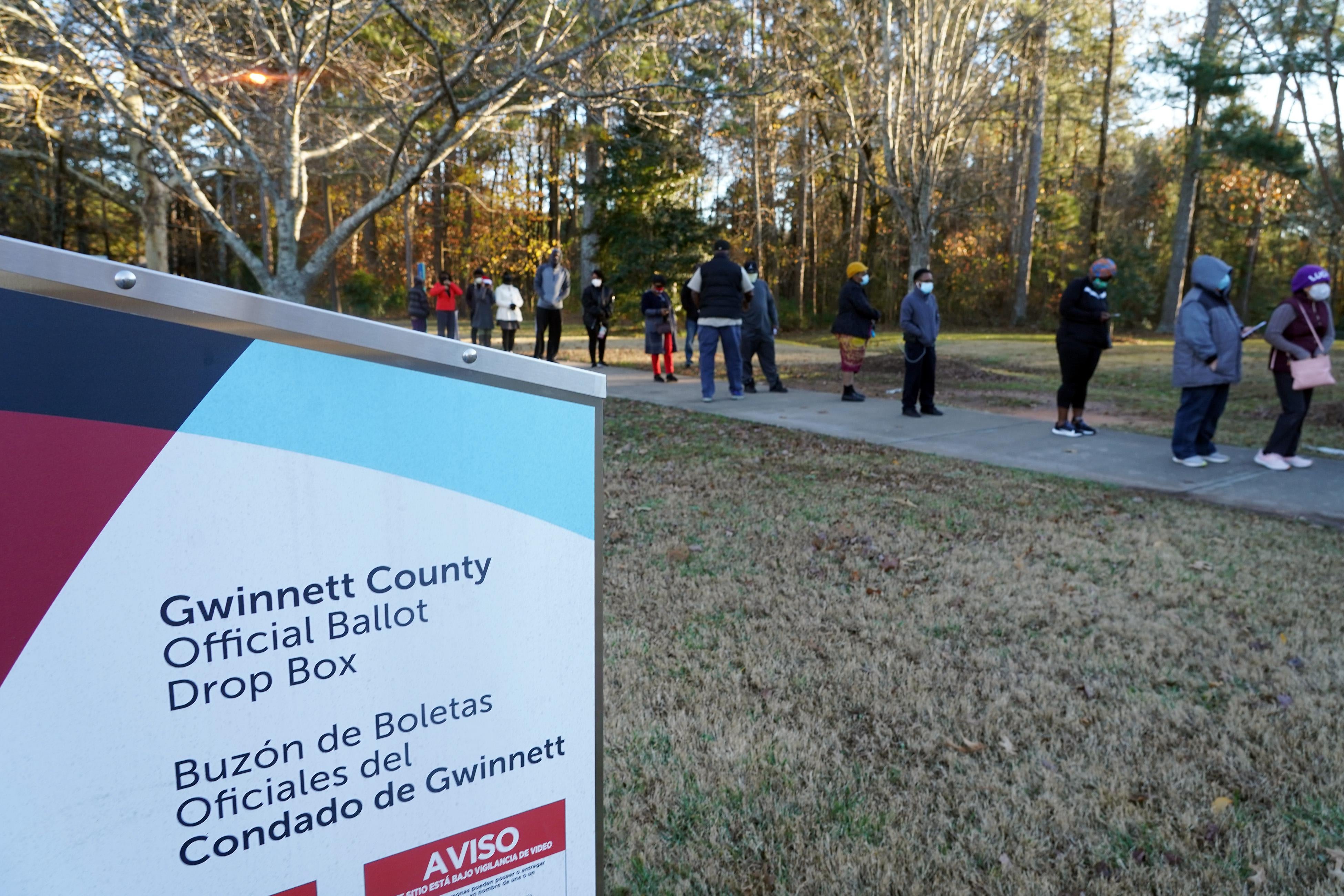 Voters stand in line outside a Georgia polling location with a ballot dropbox in the foreground.