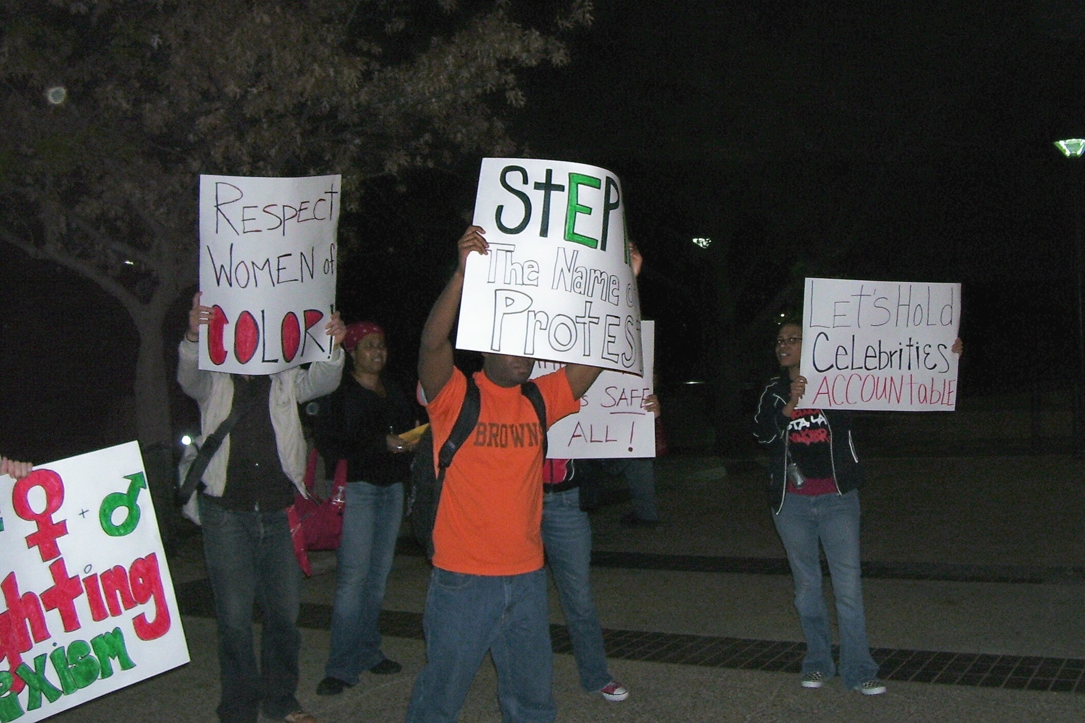 A group of students hold protest signs that say messages like "Let's hold celebrities accountable" and "Respect women of color."