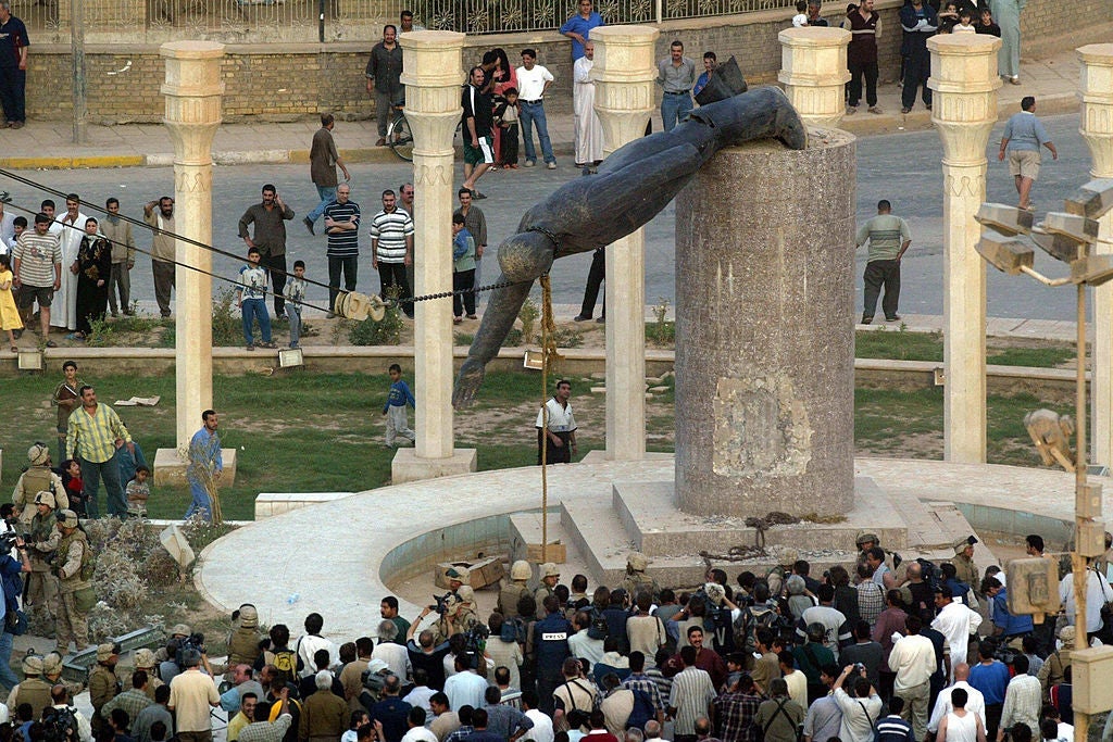 A crowd, seen from above, watches as American soldiers pull a statue of Saddam Hussein off its pedestal with a rope and a chain.