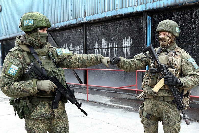 Two men in military fatigues with large guns bump fists. 