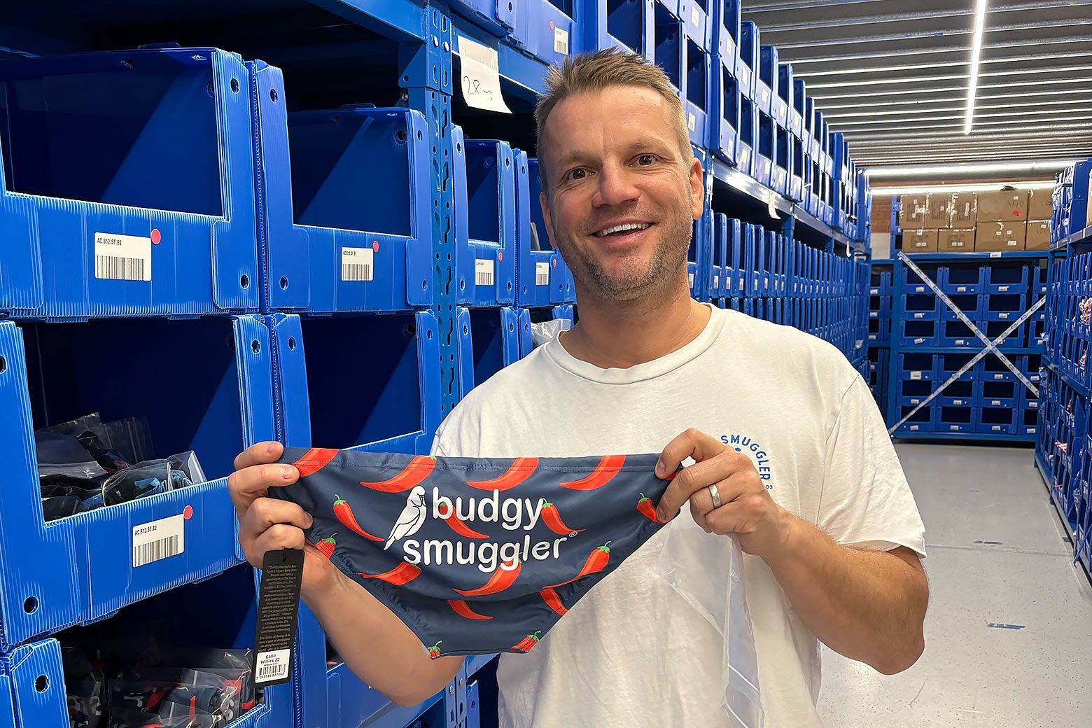 A man smiling holding a Budgy Smuggler brand of underwear.