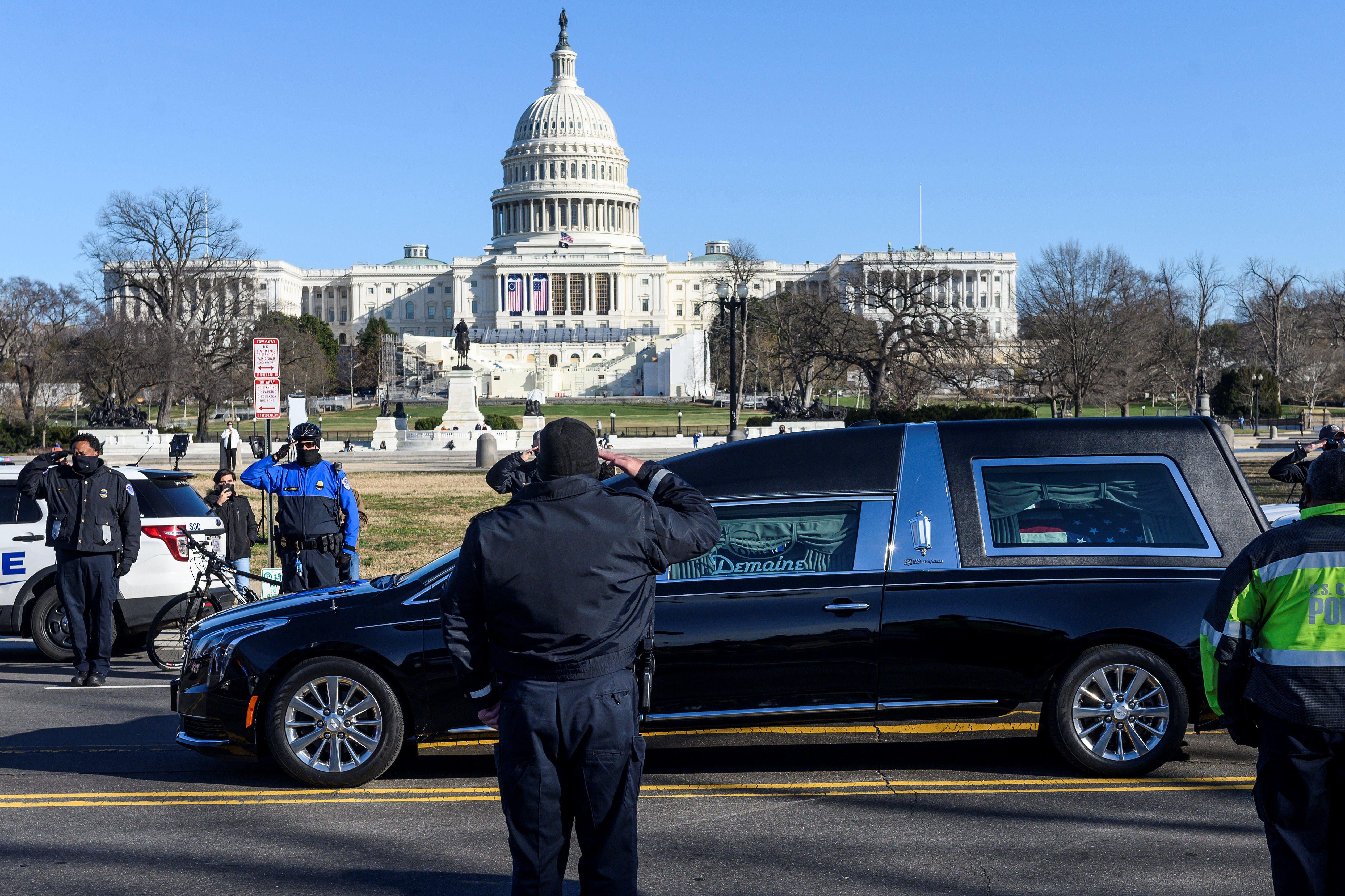 Capitol Police officers salute a hearse passing by on a road in front of the Capitol