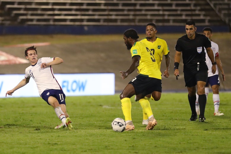 Brenden Aaronson follows through after kicking the ball, Jamaica's Anthony Grant gets a foot on it