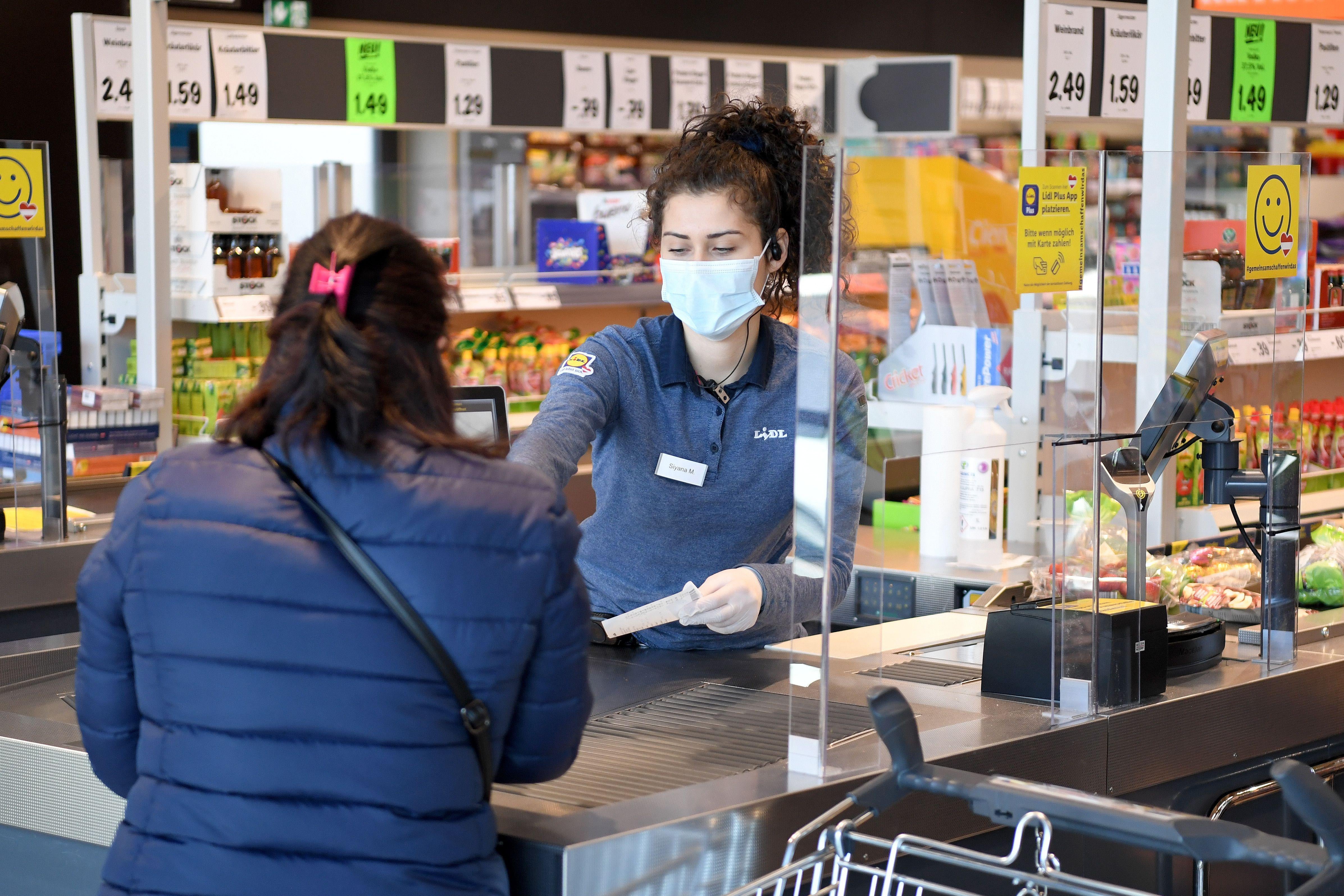 A woman behind a counter wears a mask while helping a customer.