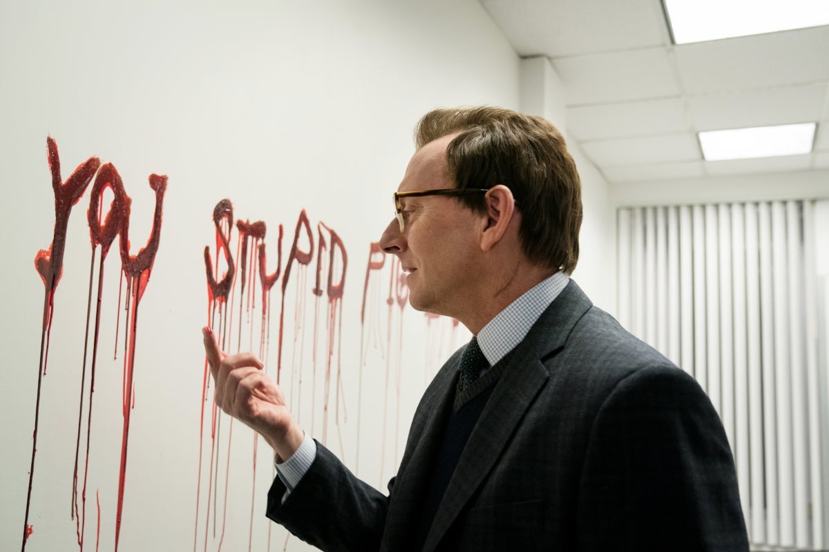 Michael Emerson, as Leland Townsend, examines red liquid on his finger. The wall in front of him is covered in dripping red letters spelling out "you stupid pig."