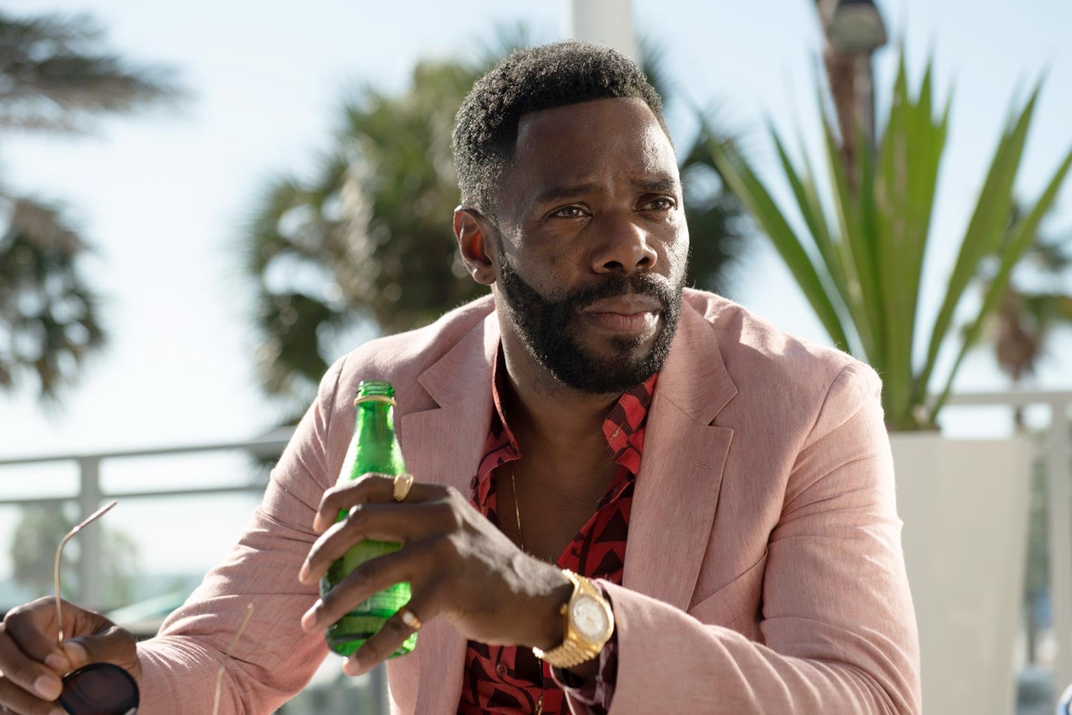 Colman Domingo wearing a pink suit and holding a sparkling water bottle.