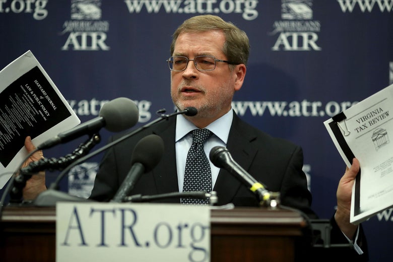Grover Norquist, at a lectern with microphones that reads "ATR.org," holds up two packets of paper.