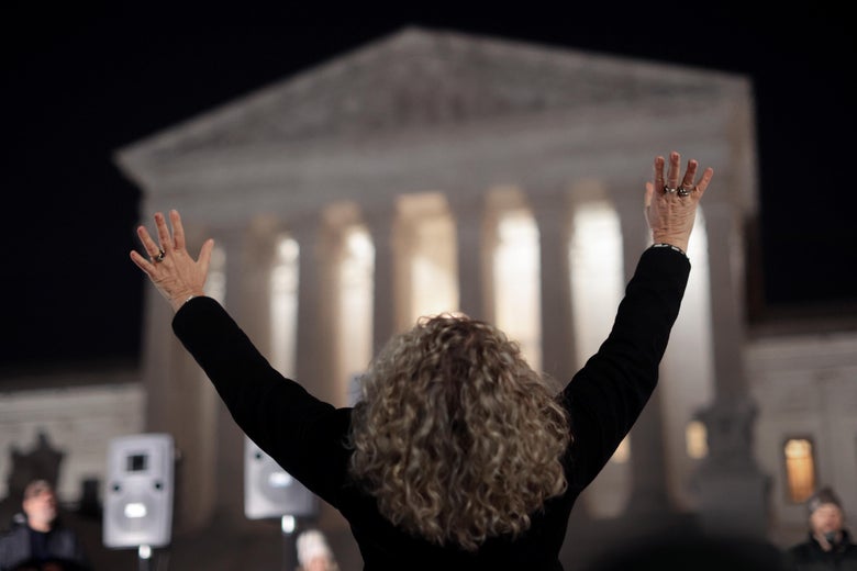 A woman with long hair raises her hands to the heavens before the Supreme Court at night
