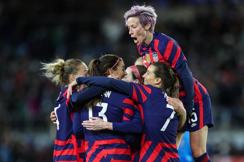 Rapinoe jumps onto the hugging cheering scrum of the team