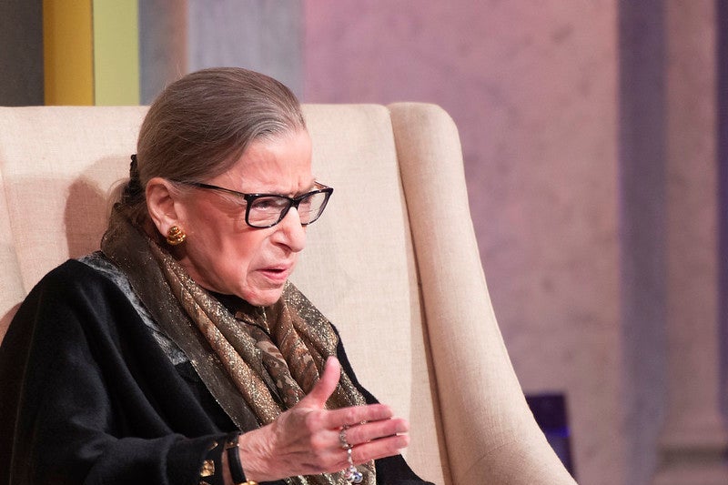 Ginsburg motions with her hand as she speaks seated onstage
