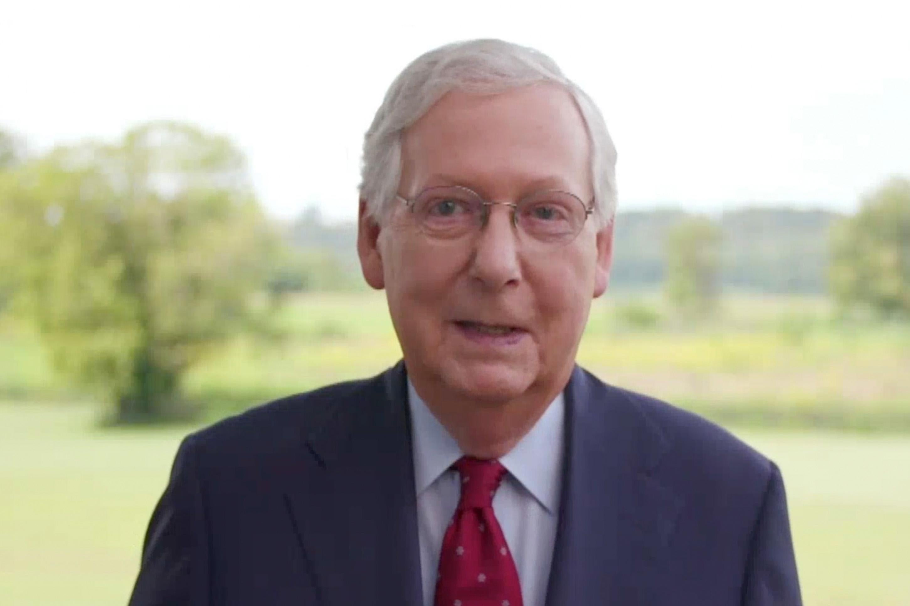 Mitch McConnell speaking into the camera with green landscape behind him.