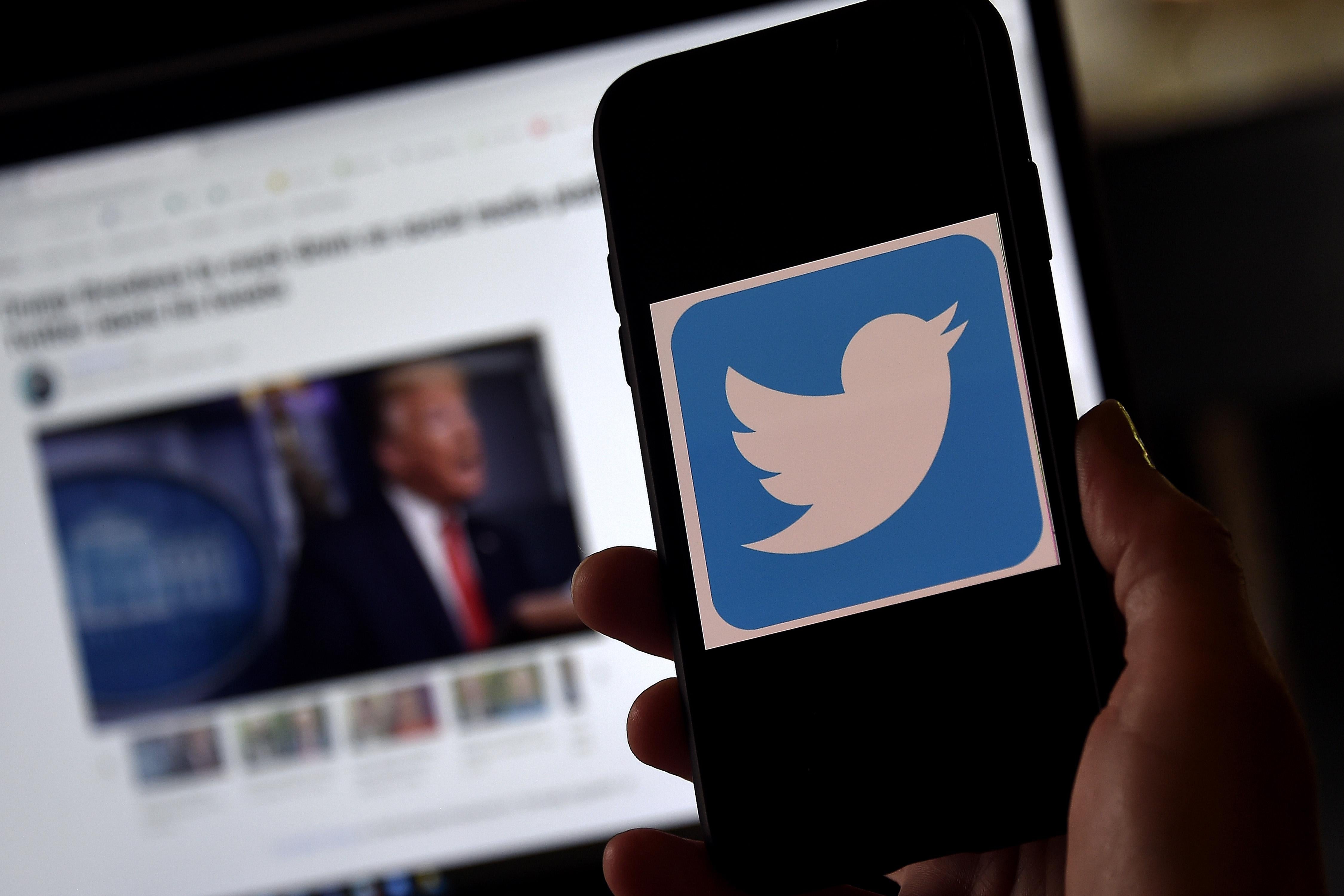 A Twitter logo is displayed on a mobile phone with Donald Trump's Twitter page shown in the background on a desktop screen.