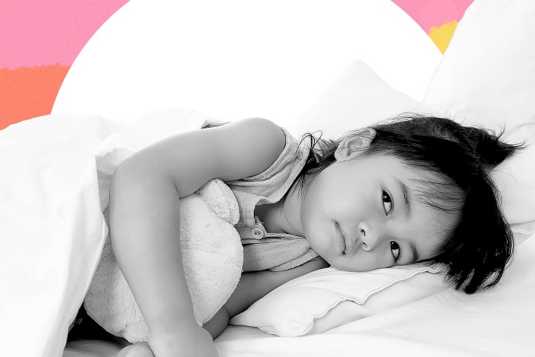 A little girl lies in bed, hugging a stuffed animal.