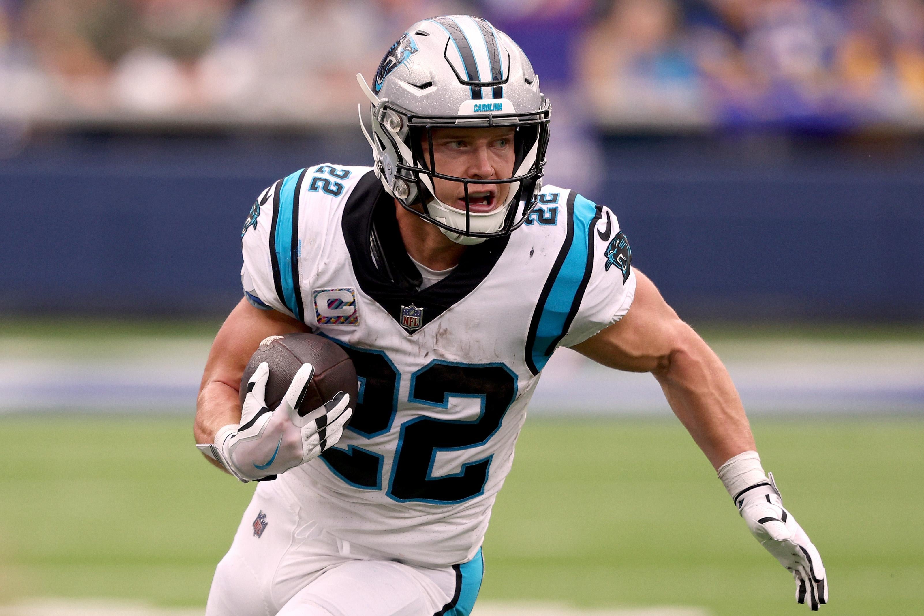 McCaffrey in his Panthers uniform on the field running with the ball tucked in his right arm