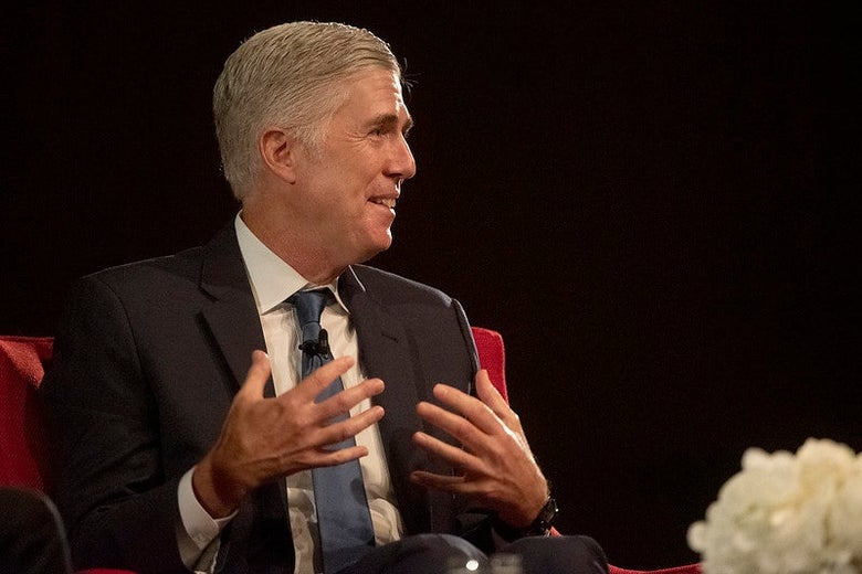 Neil Gorsuch, seated onstage, gesticulates and grins.