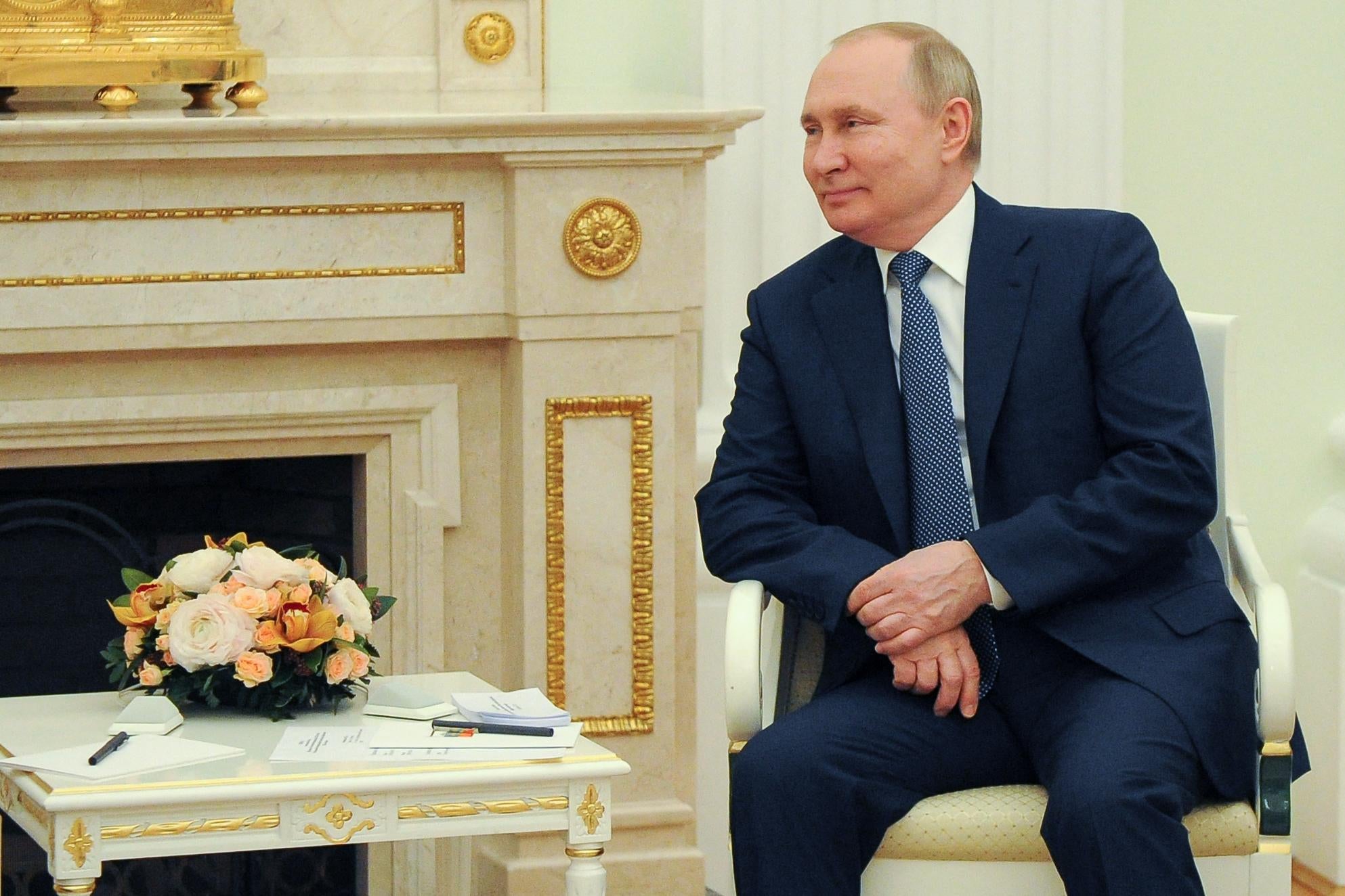 Putin smiling and leaning on one arm of his chair in a plush-looking stateroom