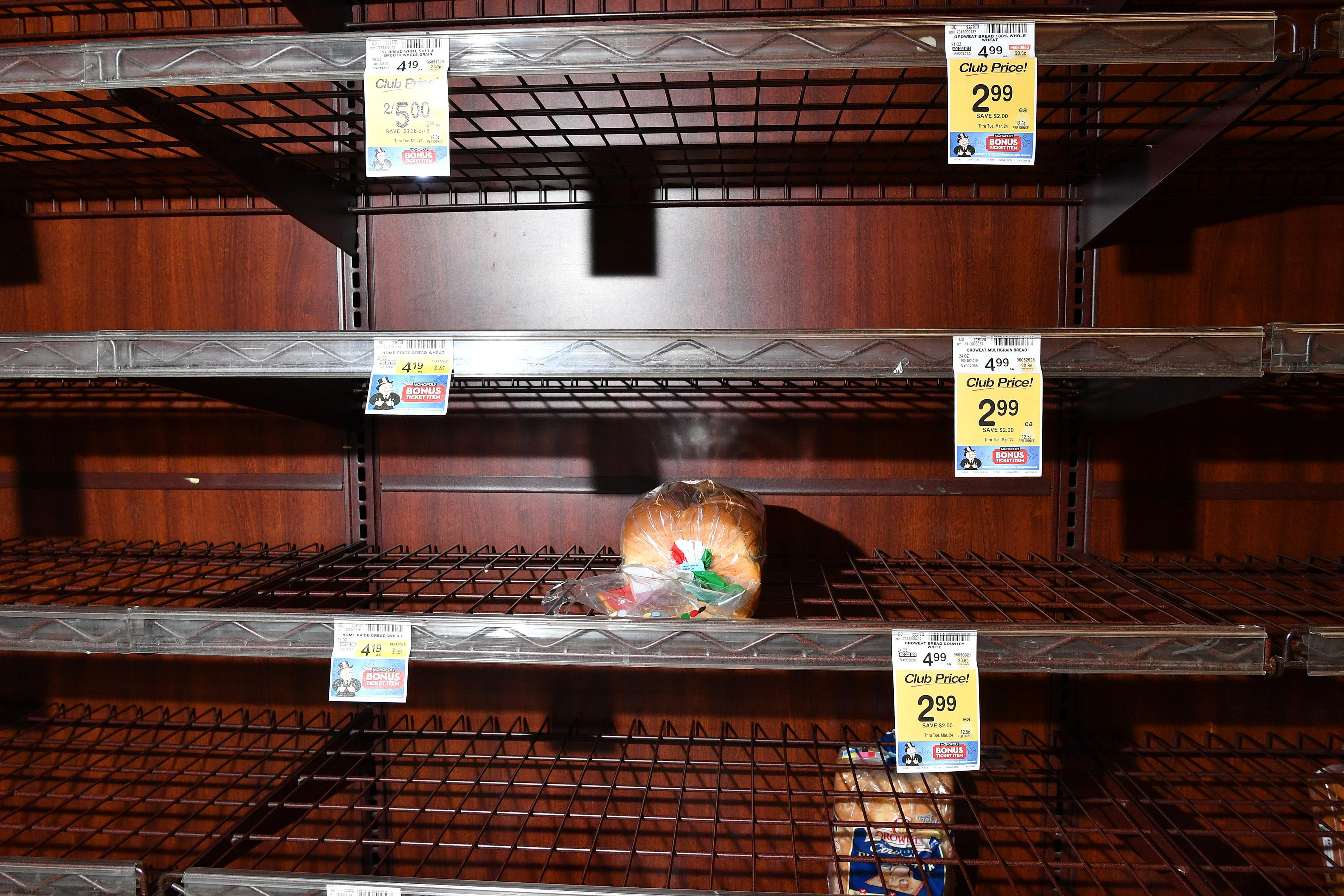 Two loaves of bread sit on otherwise empty grocery store shelves.