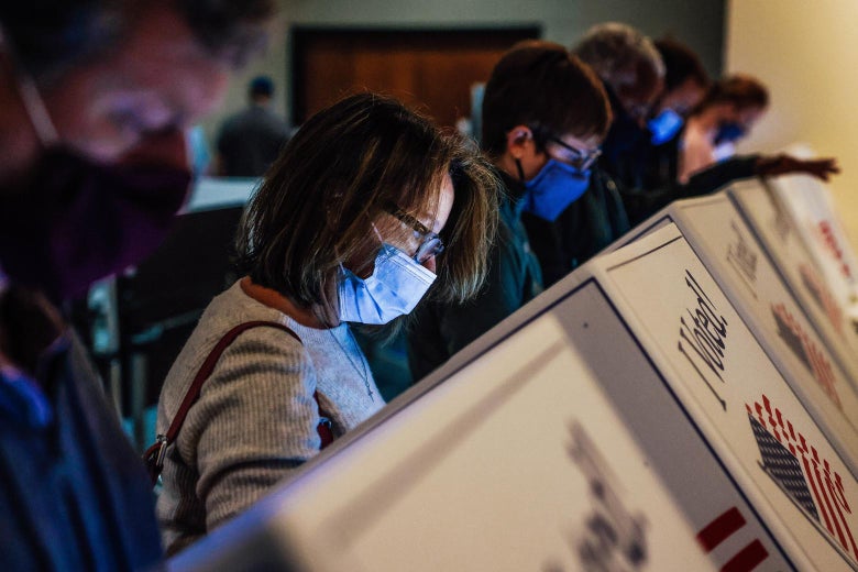 Row of people voting while wearing masks at a local library.