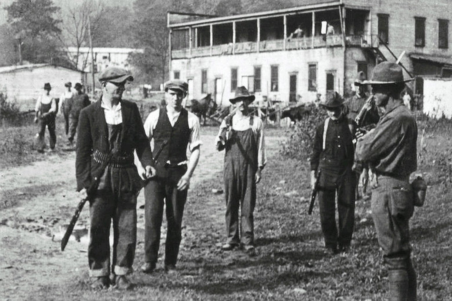 Coal miners and federal troops with weapons stand outside a building.