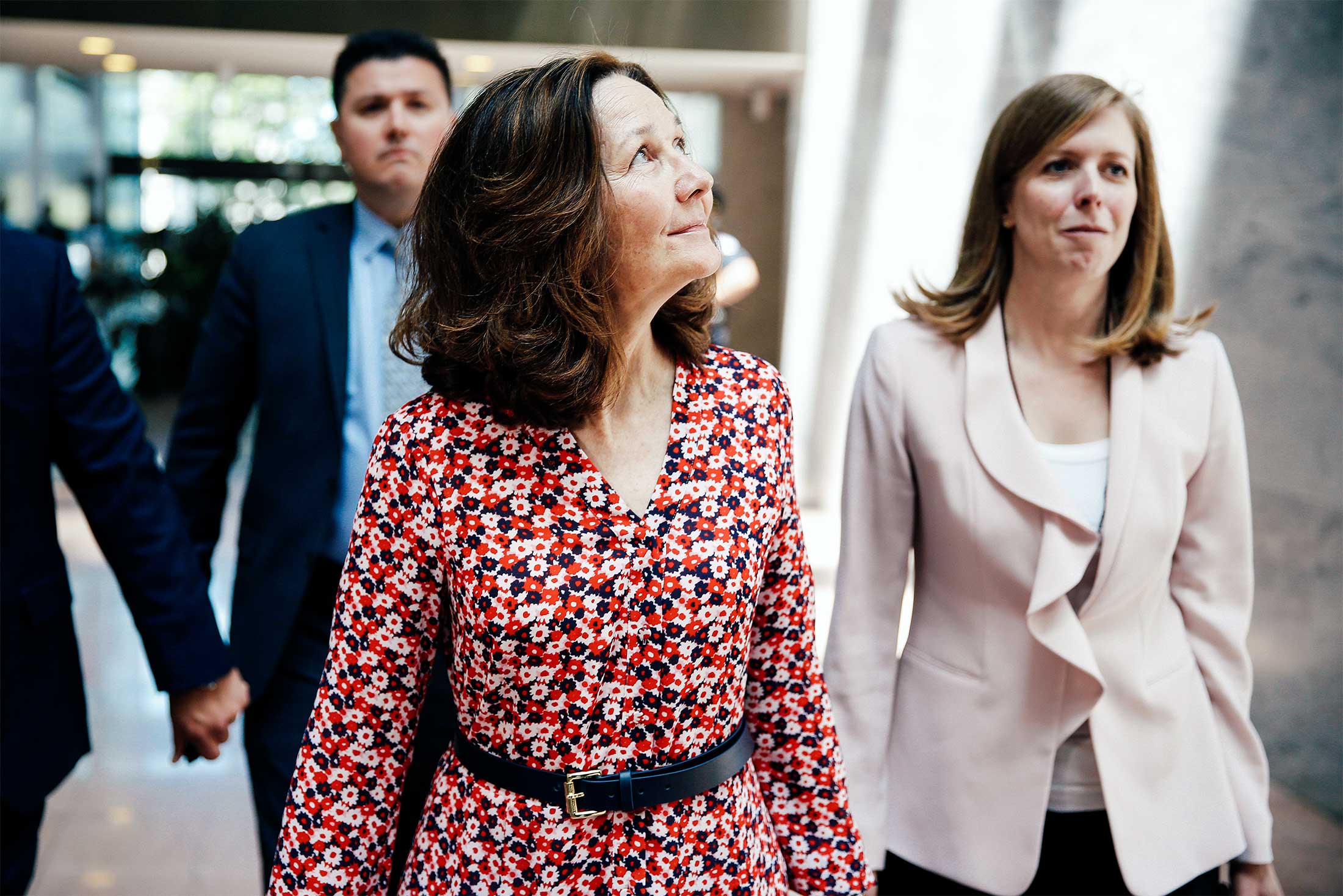 Gina Haspel walks through a Senate office building while wearing a flowery red dress.