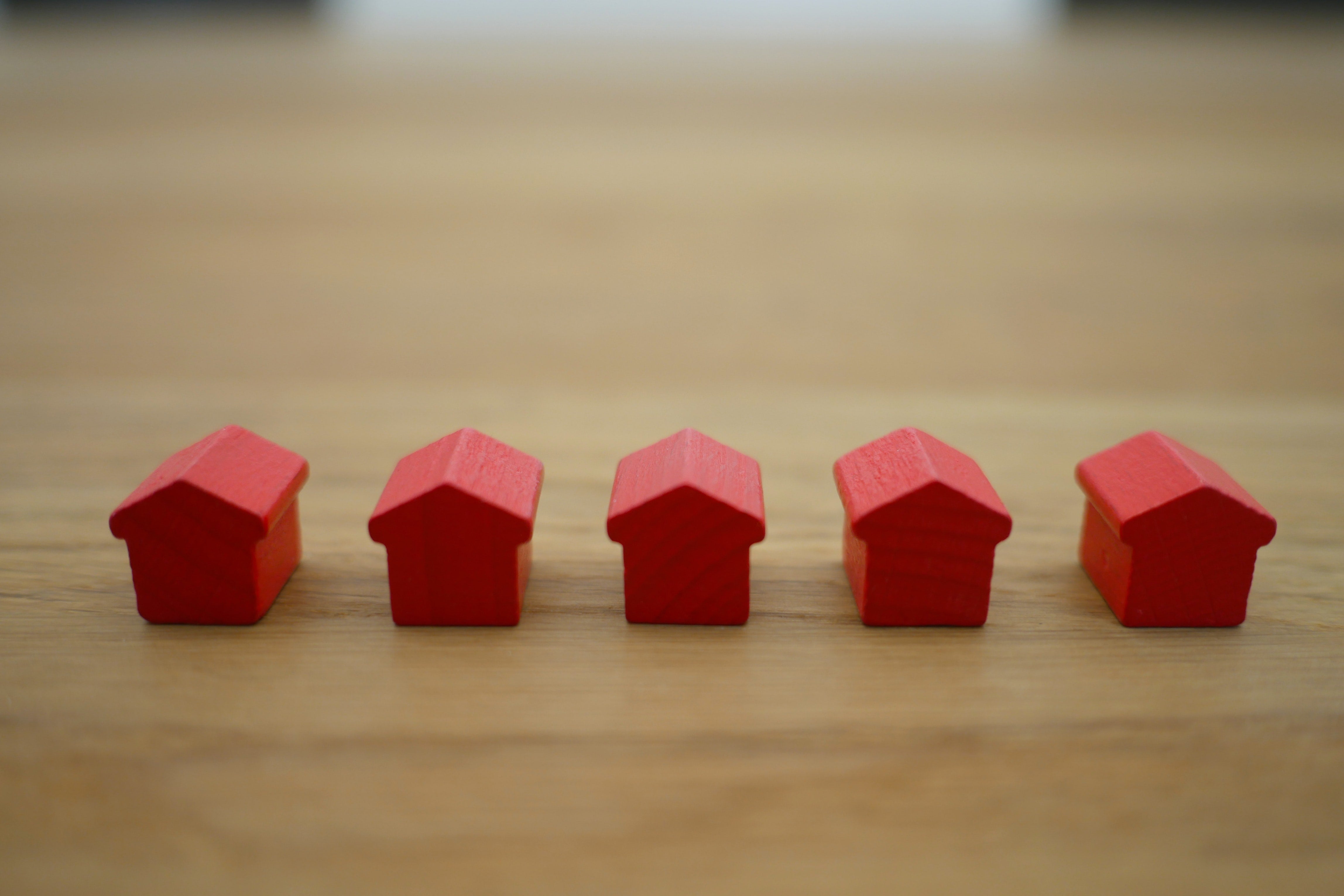 Five small red toy houses lined up on a wooden counter.