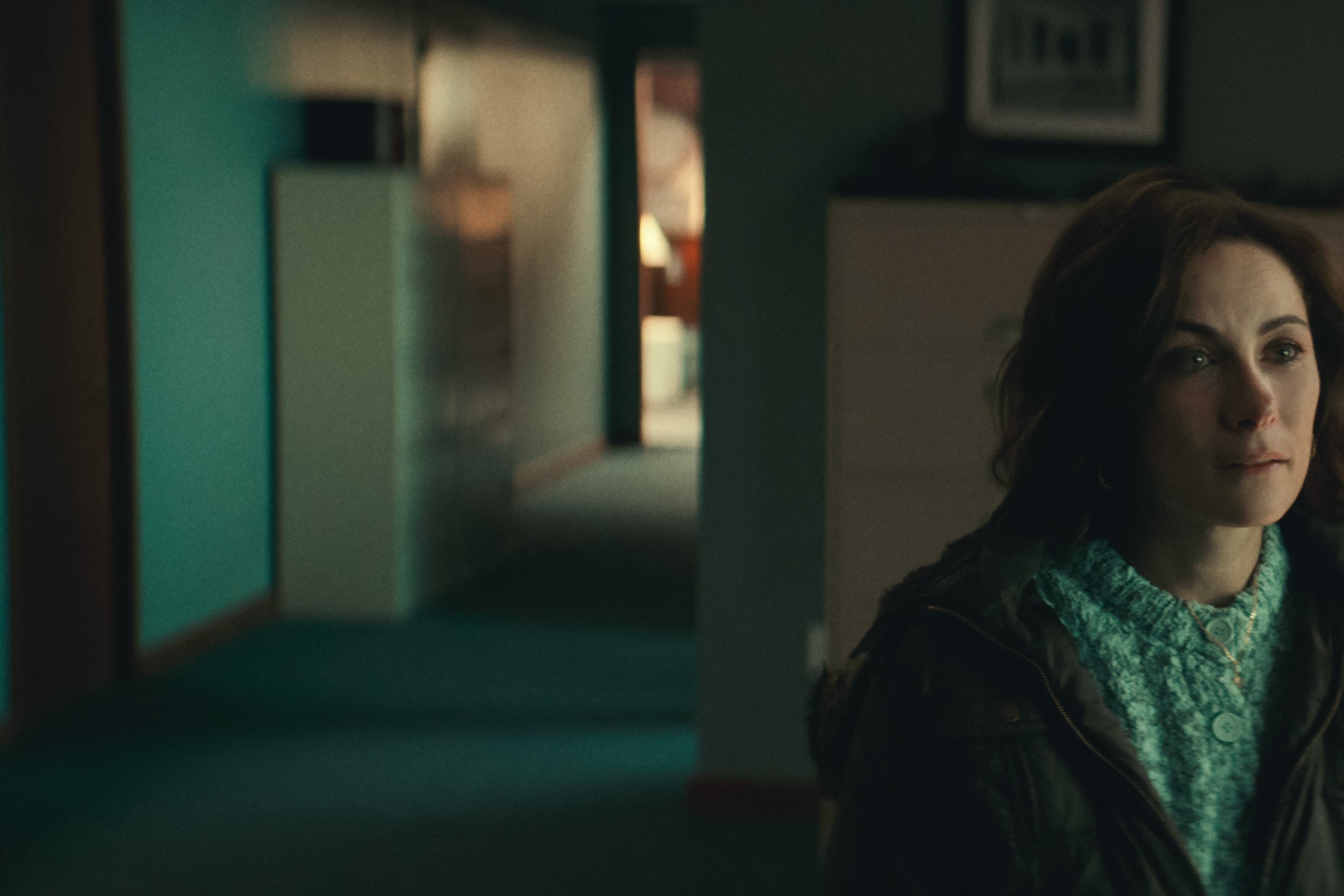 Benanti sits in a coat and sweater in an office. Behind her, an early-2000s computer.