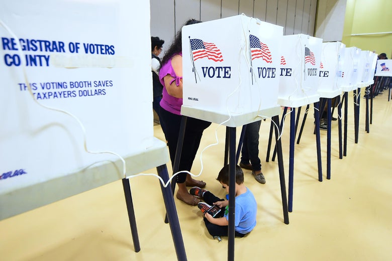A woman votes at a booth as her child plays with a cellphone below.