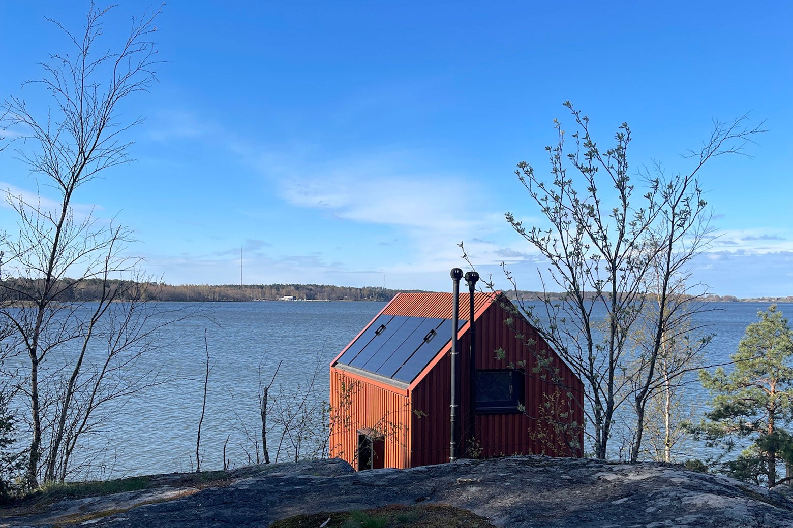 A red cabin on the shore of a lake.