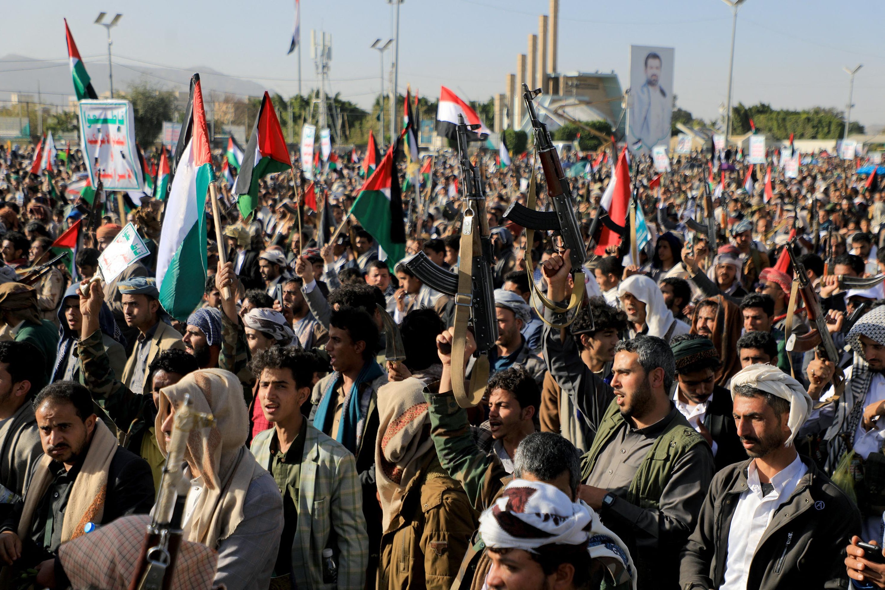 A large group of people, some holding Palestinian flags and guns in the air.