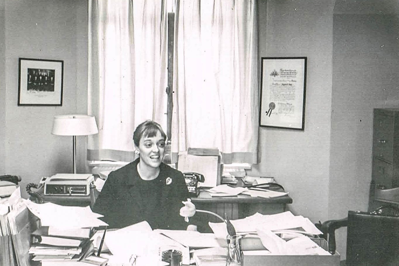 Virginia Davis Nordin sits at a desk piled high with papers.