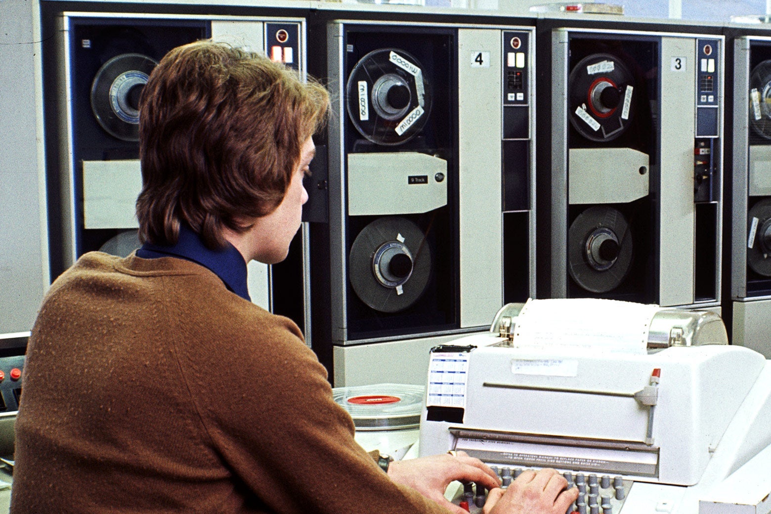 A man types on a big old-fashioned mainframe computer.