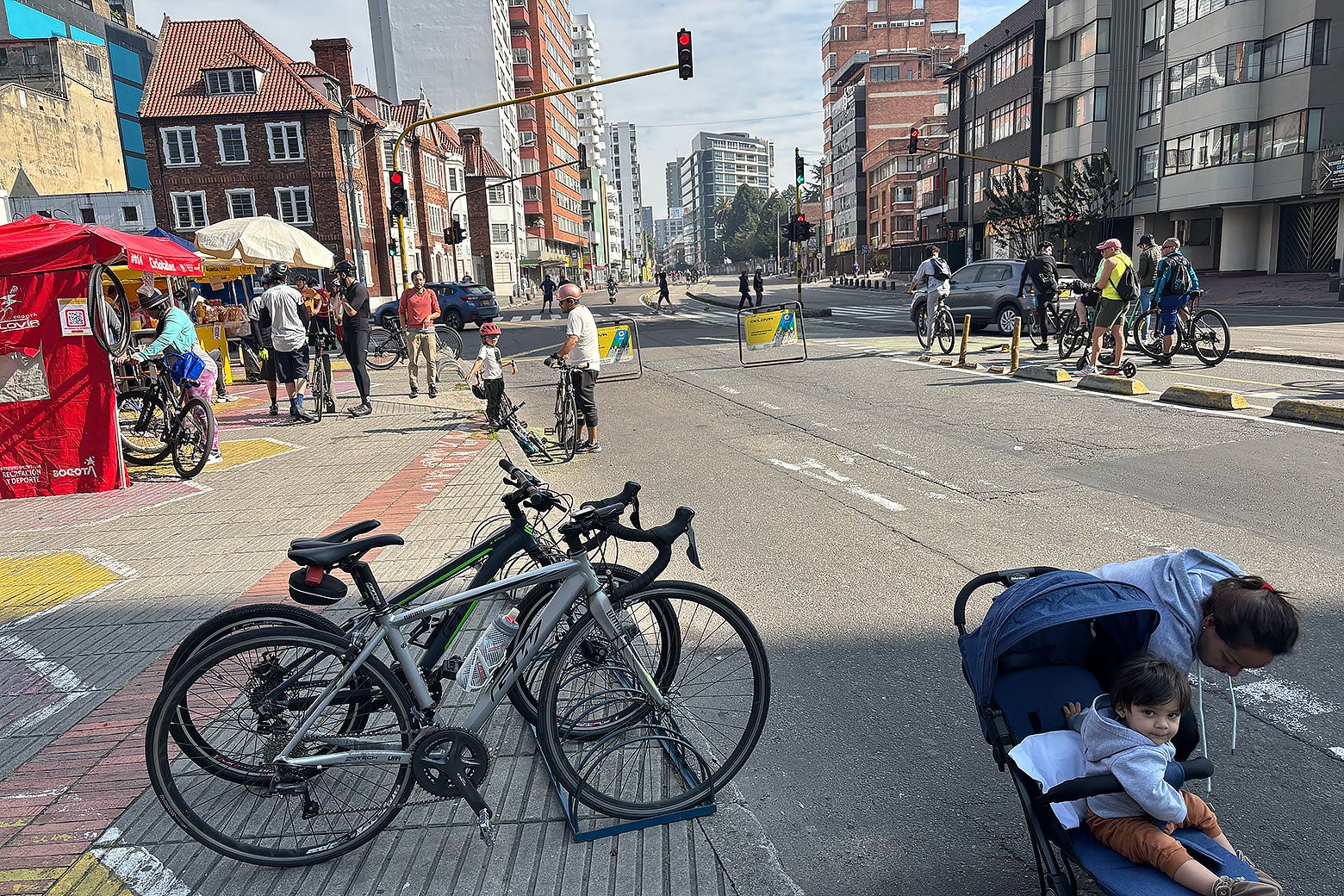 Some bikes are parked and people are at red tents buying food while other bike past.