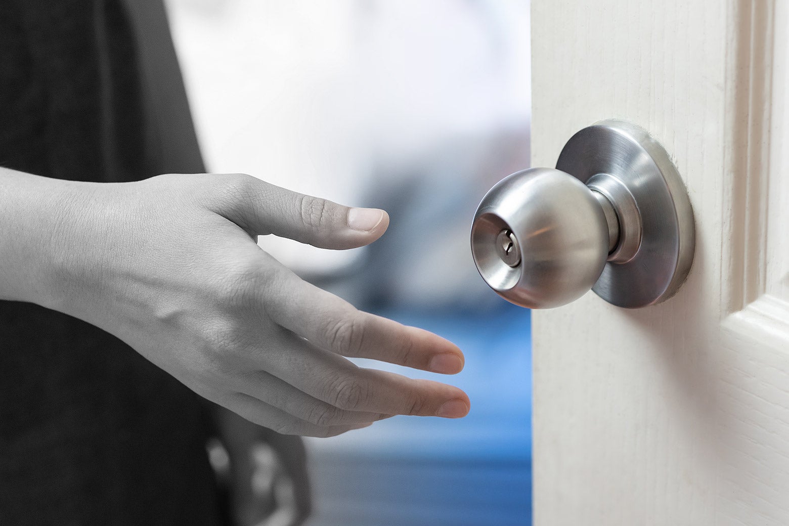 A hand reaching for a doorknob, with half of the image in black and white