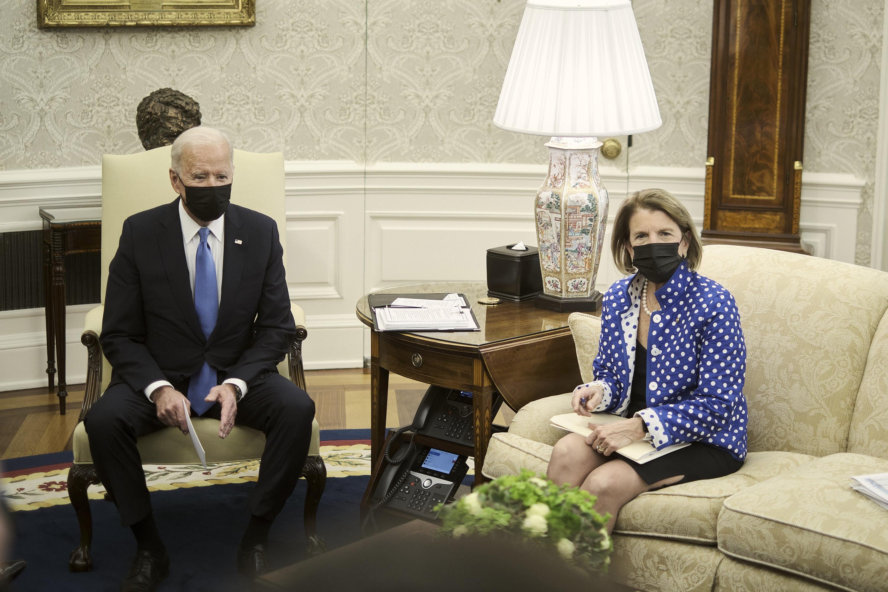 Biden sits in an armchair and Capito on a couch, both wearing black masks, during a meeting