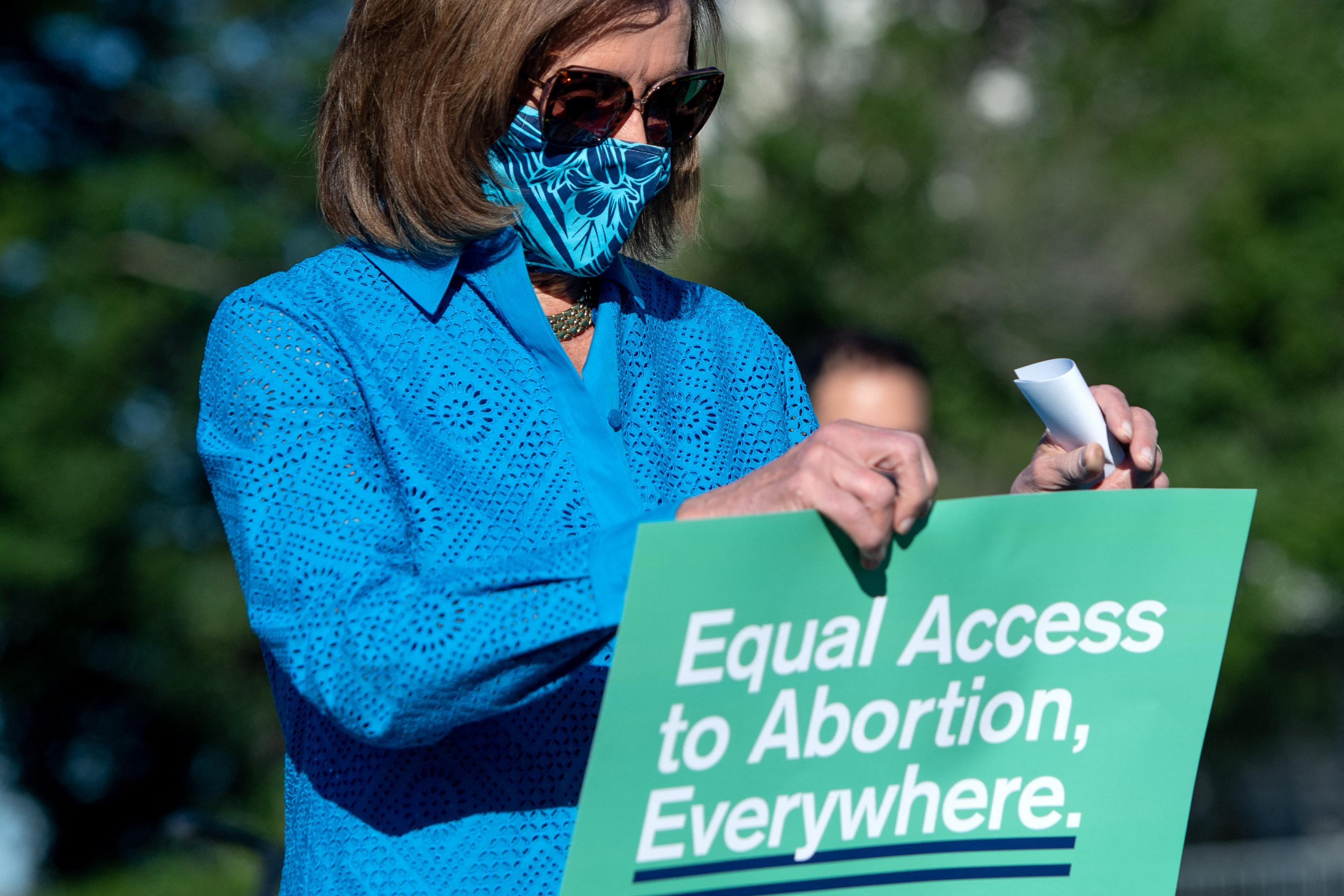 Pelosi stares at a sign that reads "Equal Access To Abortion, Everywhere."