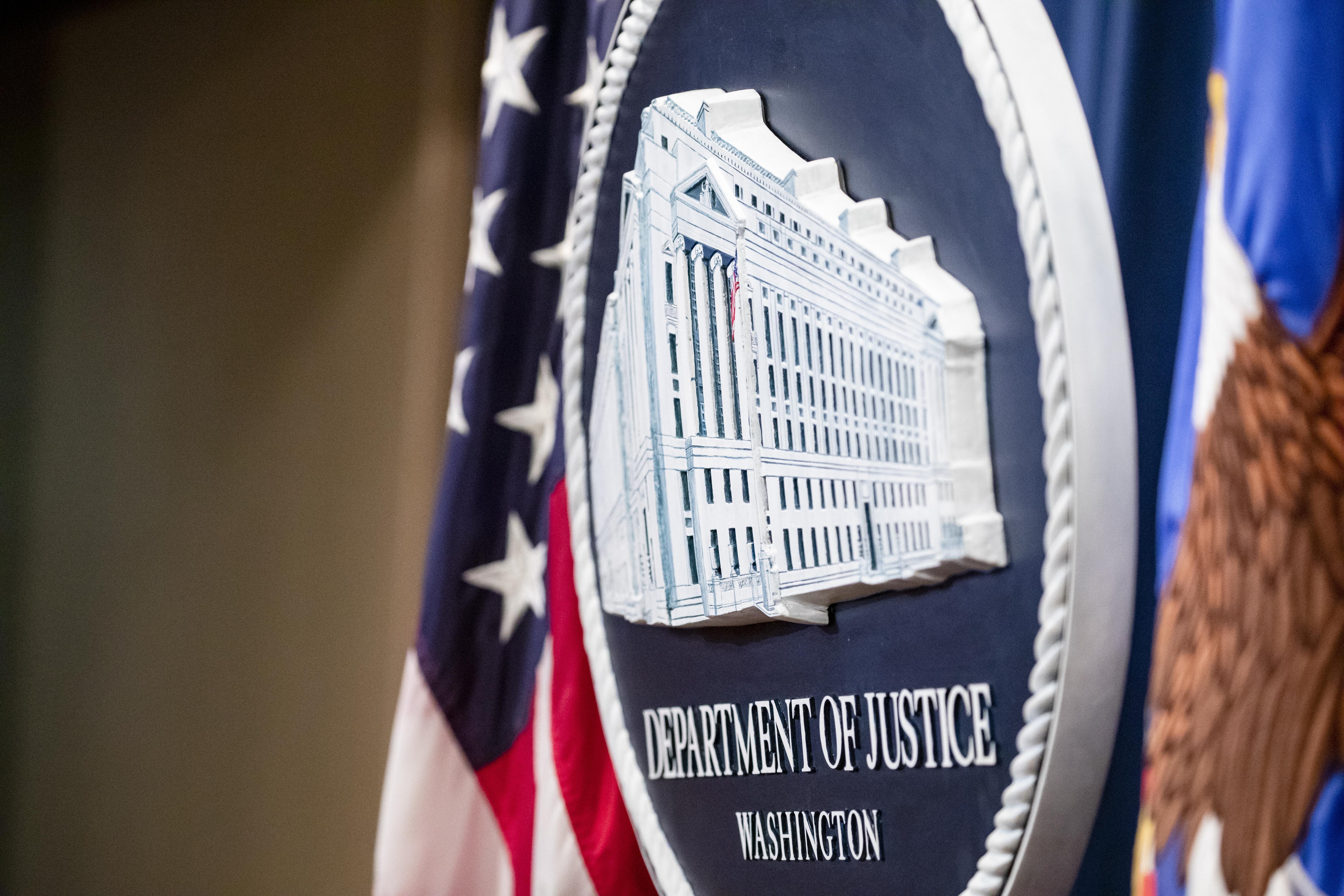 The Justice Department seal, seen at an angle between two U.S. flags