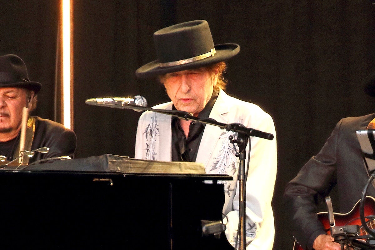 Bob Dylan wears a black hat and plays piano.