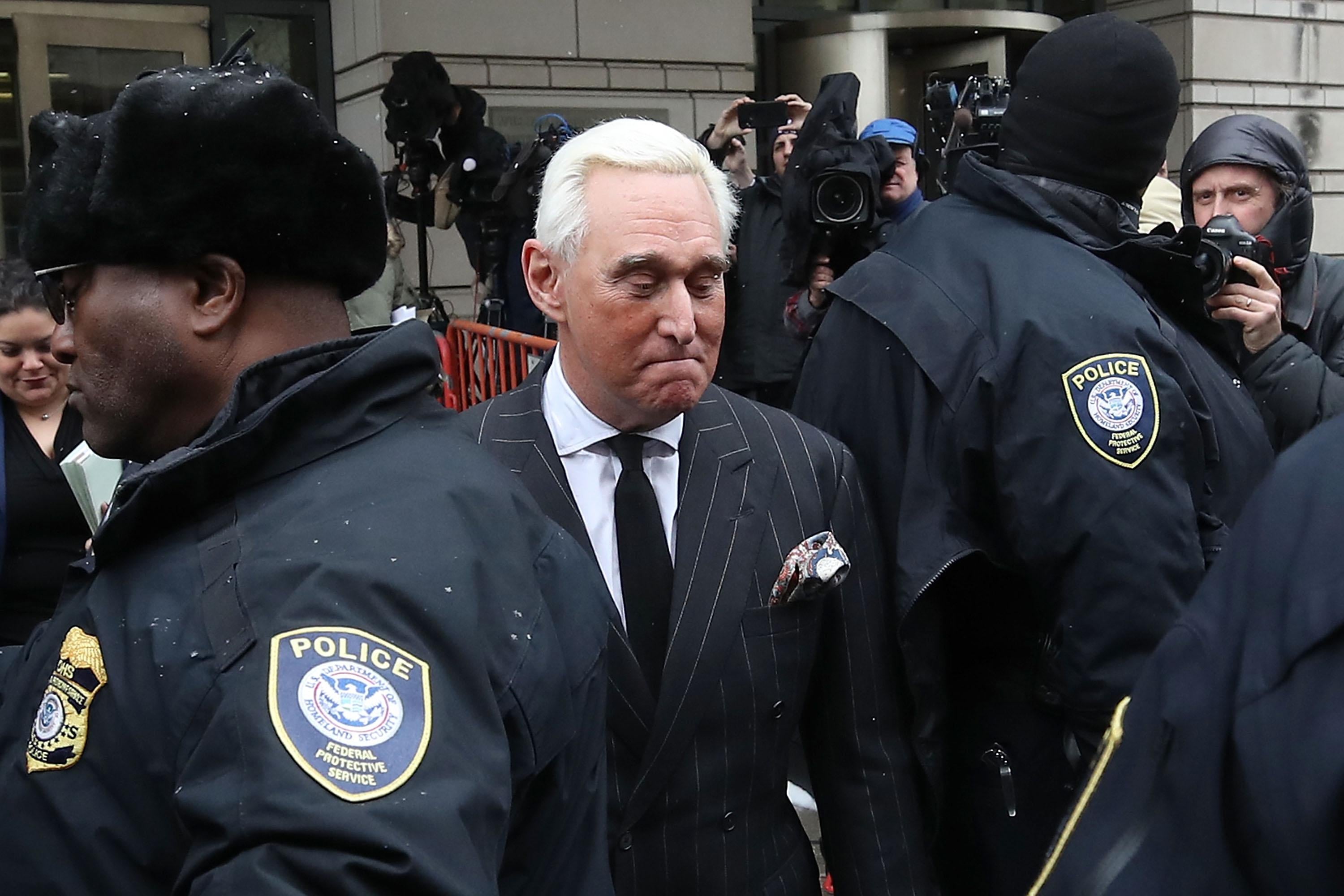 Roger Stone glances downward as he moves through a crowd of police and media in front of the courthouse.