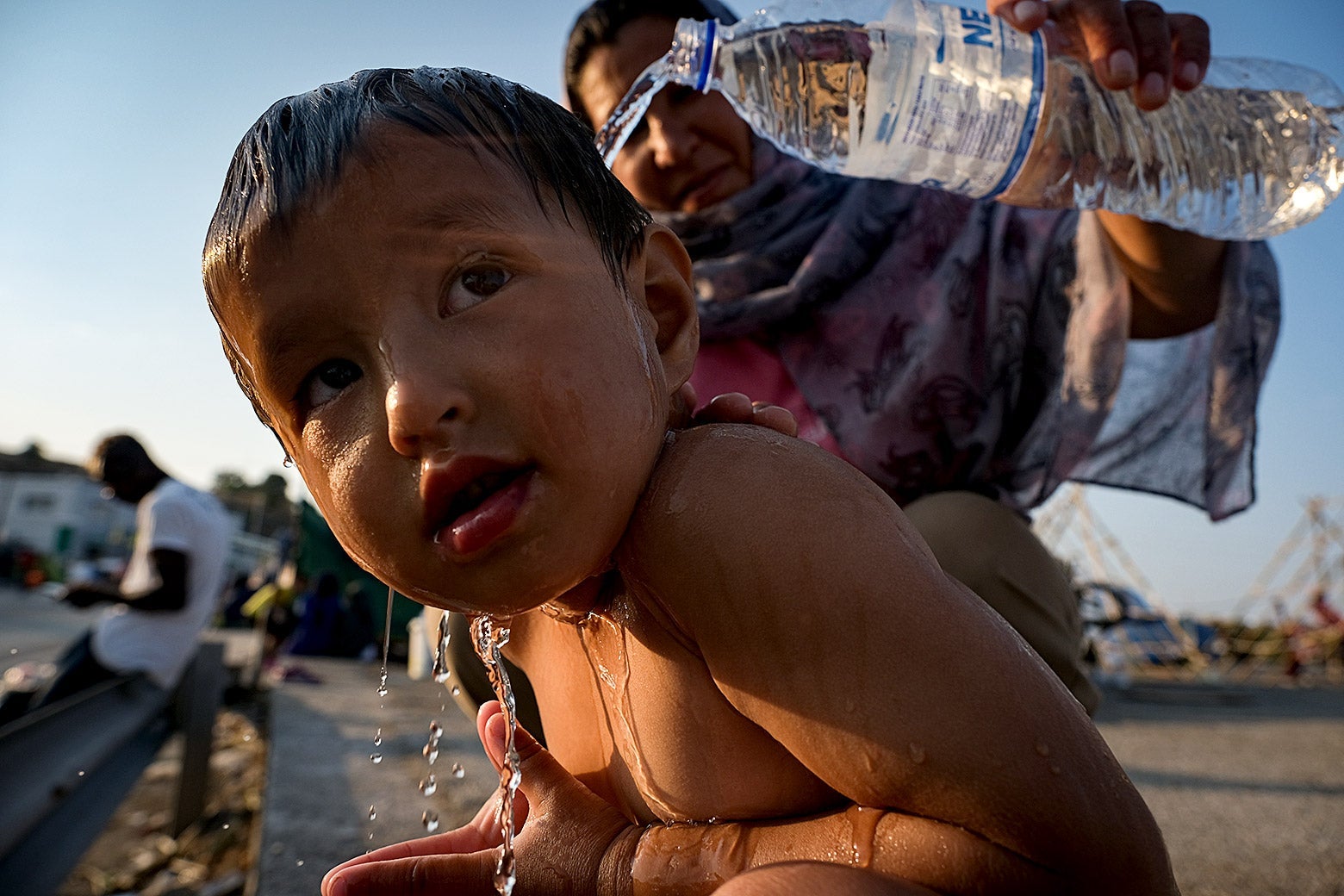 A woman pours water from a plastic water bottle onto a child.
