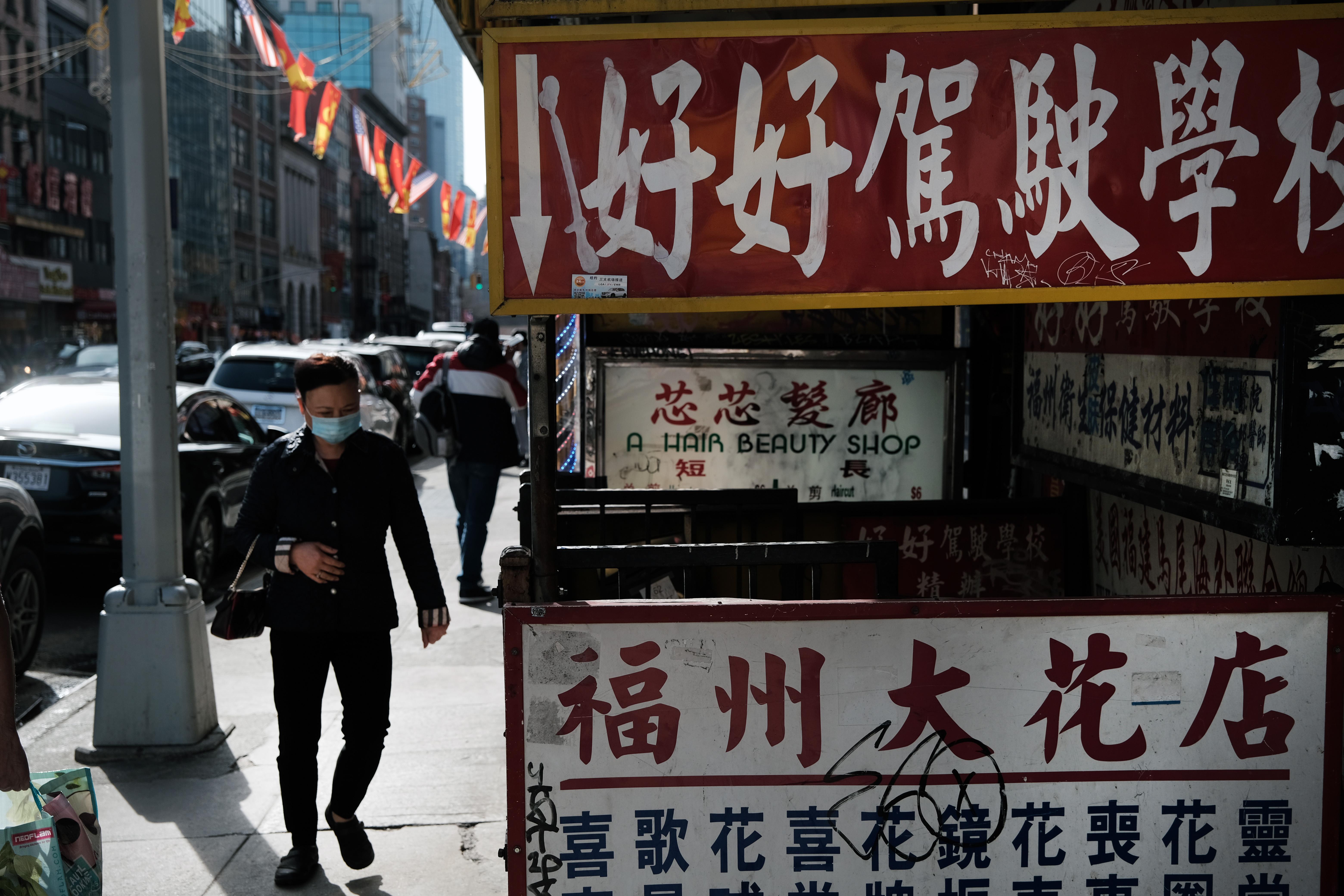 People walk on a sidewalk in Chinatown past signs in Chinese