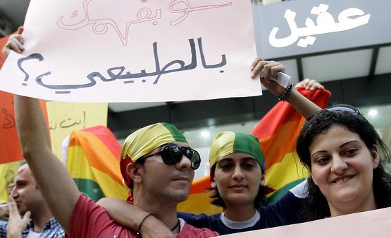 Lebanese protesters wearing rainbow-colored bandanas hold a sign reading in Arabic.