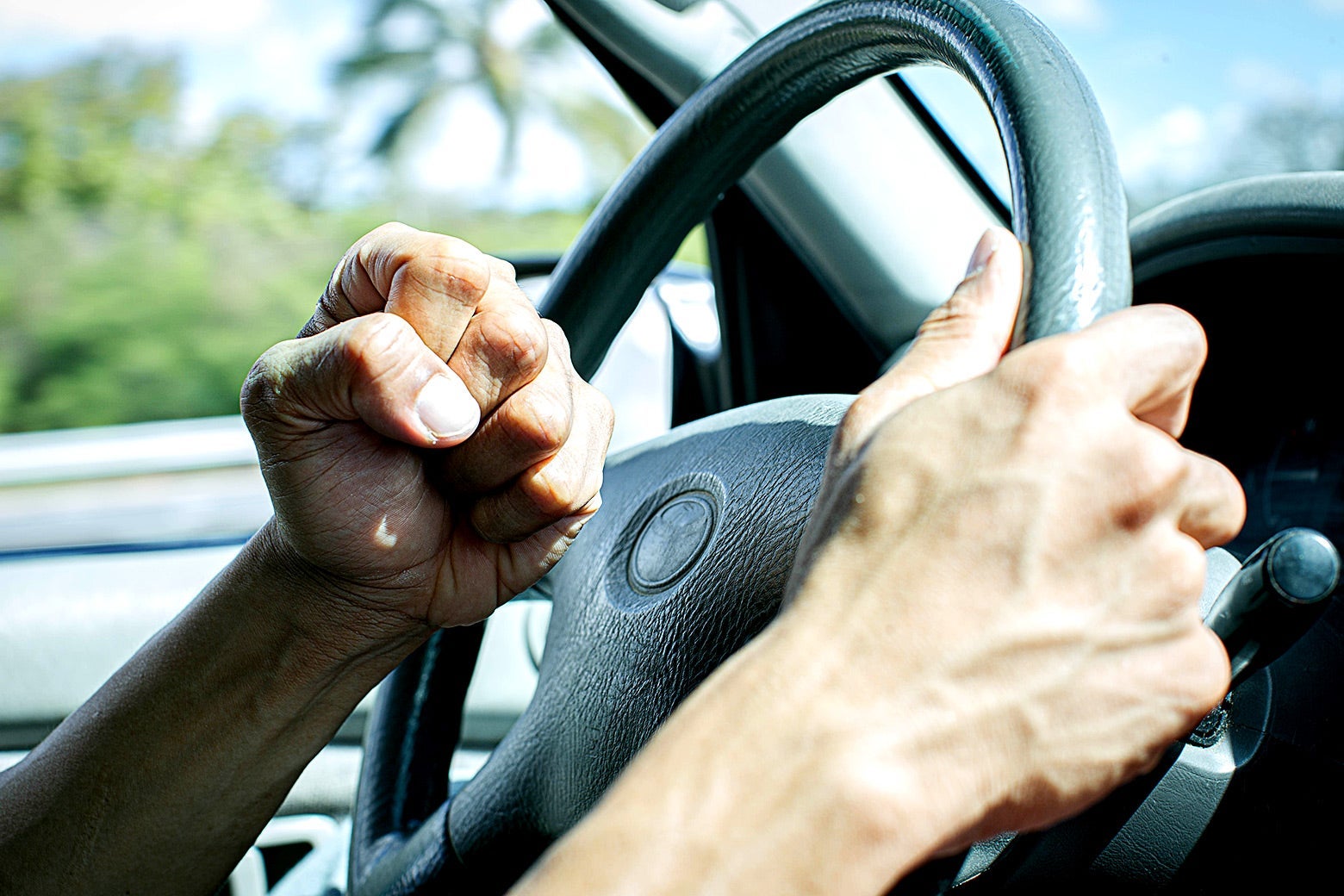 A frustrated driver holding a steering wheel w/ his right hand and a clenched left fist.