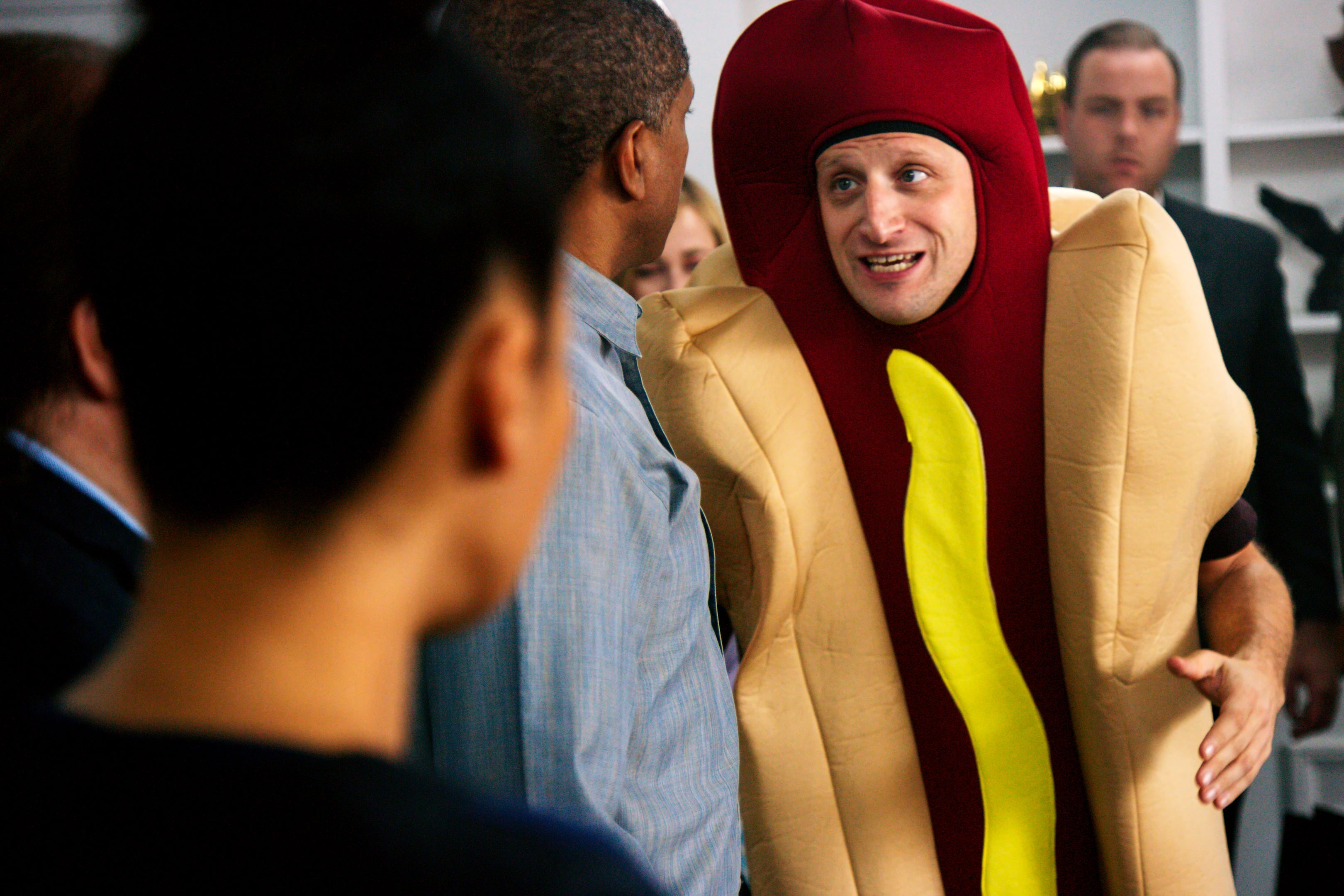 Tim Robinson stands in a crowd of people wearing a hot dog costume.