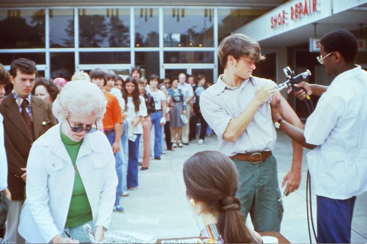 A man gets a vaccine shot while others stand in line waiting.