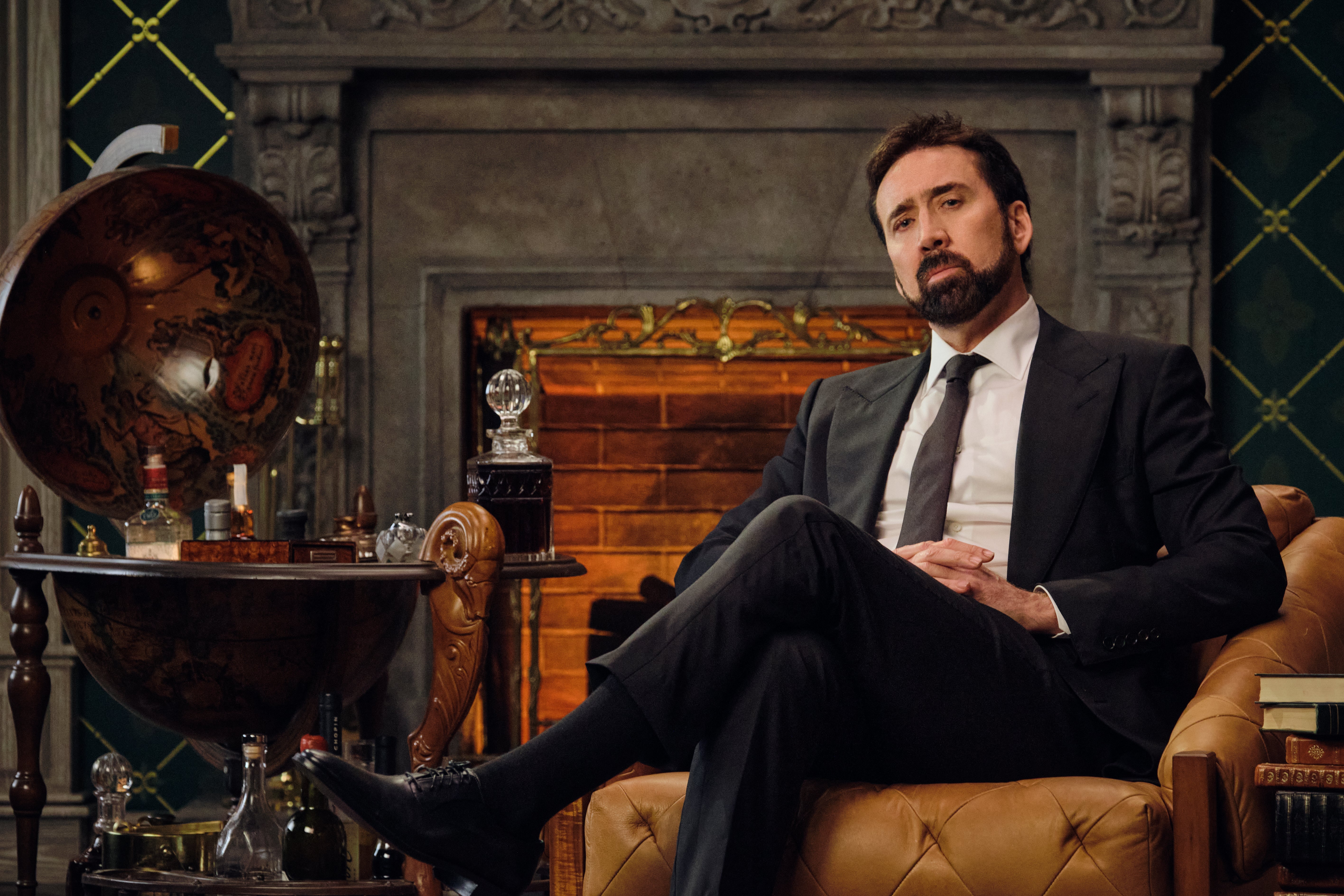 Nicolas Cage reclines in an armchair by a fire.