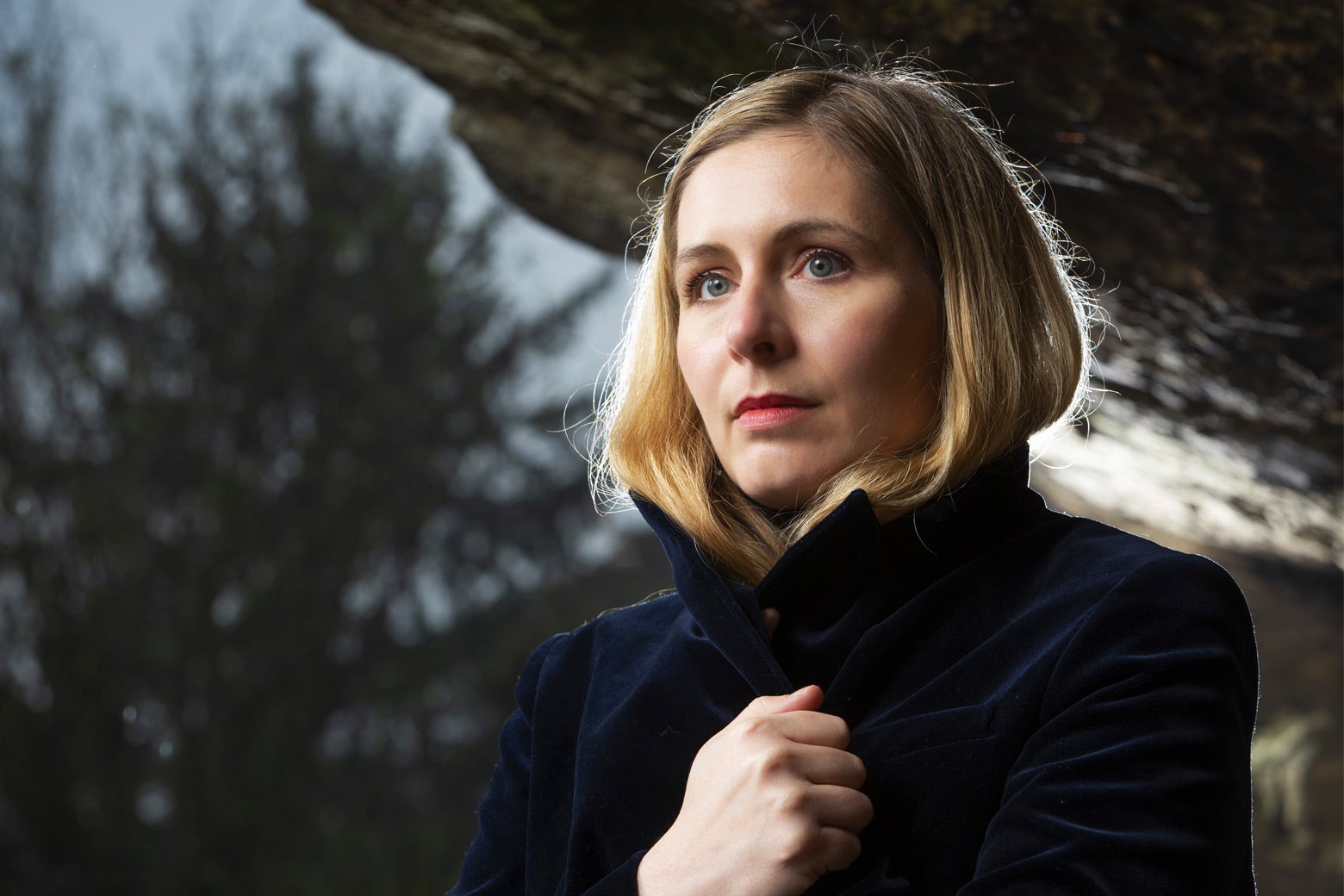 A woman with blond hair stands with her coat pulled up around her neck.