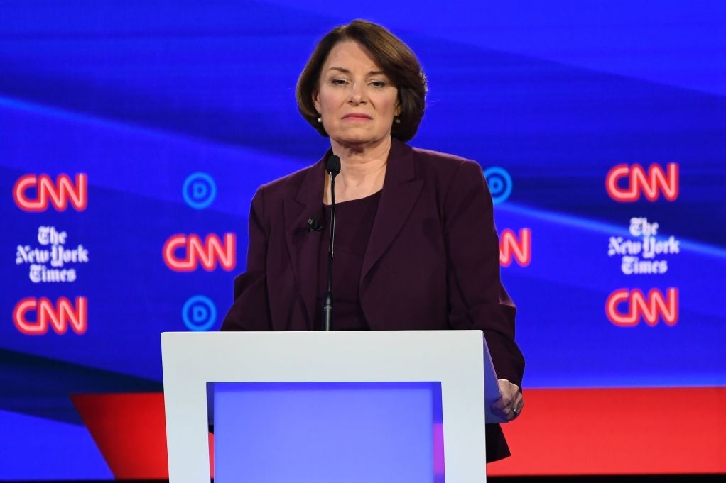 Amy Klobuchar frowns while holding a debate lectern.