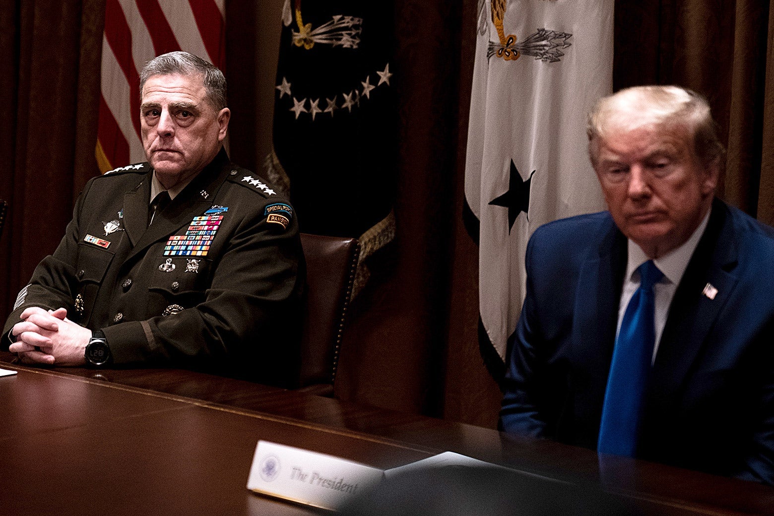 Mark Mille­y sits at a table with Trump. Milley's hands are folded on the table and he is in military uniform. Trump is wearing a suit.